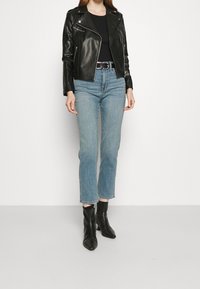 Chaqueta de motorista de cuero negro con detalles de cremallera, combinada con jeans rectos de color azul claro y ankle boots negros puntiagudos.