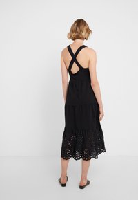 Černé bezramínkové šaty s vrstveným designem, s výřezovými květinovými detaily na lemu a křížovými ramínky na zádech. Hladká bavlněná tkanina.