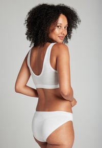 Bralette blanca de algodón con tirantes anchos, espalda redonda y braguitas de bikini blancas a juego. Textura suave, diseño simple y detalles mínimos.