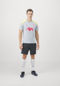 Gray short-sleeve soccer shirt with yellow accents, red "AXA" logo, and Liverpool FC emblem; paired with dark shorts and white socks.
