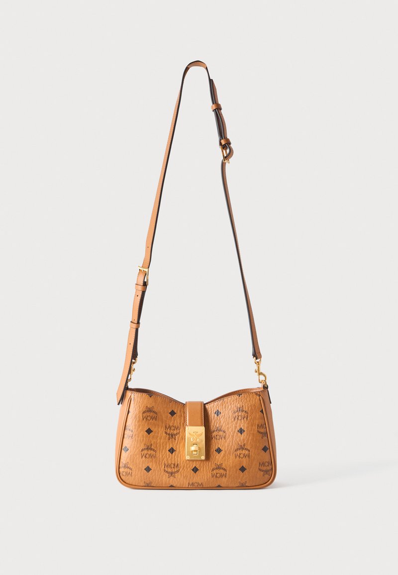 Sac bandoulière en cuir marron clair avec bandoulière réglable, fermoir doré, et motif répétitif du logo MCM sur une surface texturée.