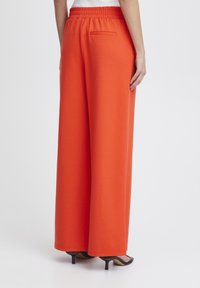 Vida orange byxor med vida ben och elastisk midja, slät textur och en bakfickdetalj. Kombinerat med svarta sandaler med öppen tå.