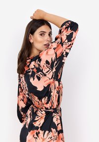 Schwarzes Kleid mit großen pfirsichfarbenen Blumenmustern, langen Ärmeln, einem entspannen Schnitt und einem Taillengürtel, das eine glatte, glänzende Stofftextur präsentiert.