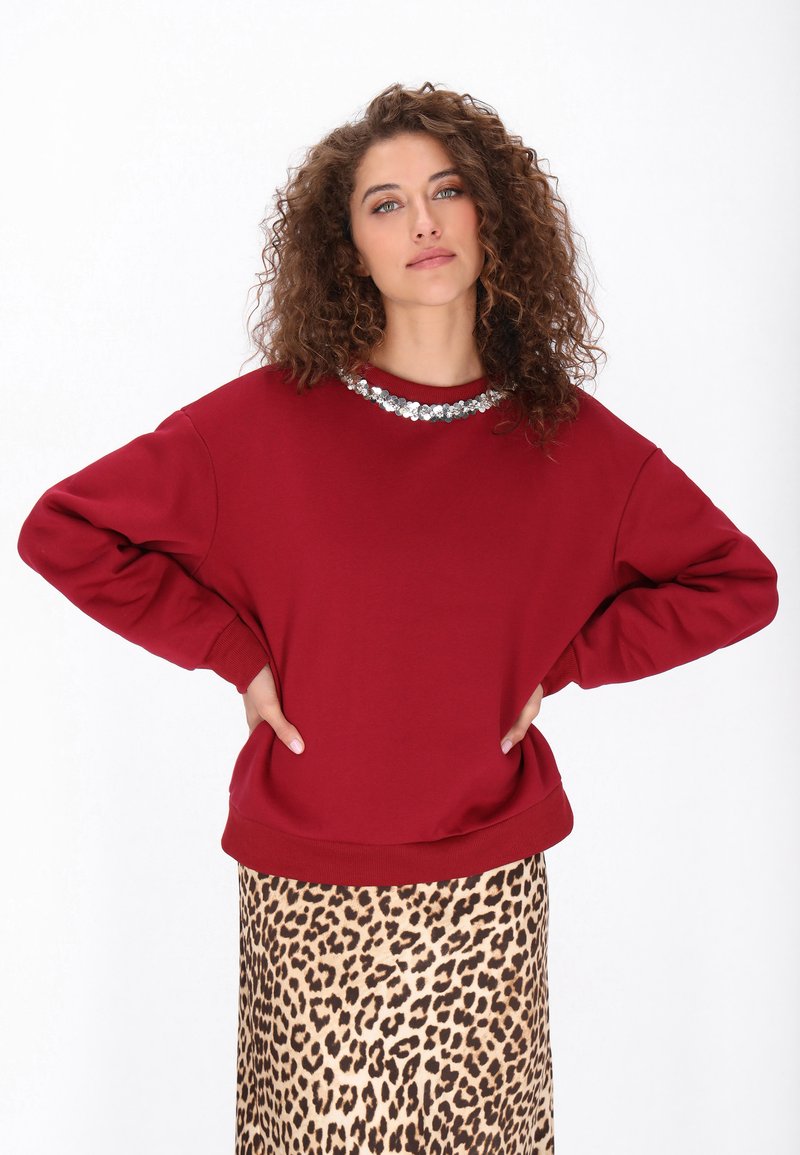 Sudadera burdeos con cuello redondo, cuello adornado con cuentas plateadas y ajuste holgado, combinada con una falda de estampado de leopardo.