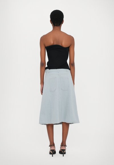 Black strapless top, light blue denim A-line skirt with frayed hem, two back pockets, model wearing black strappy heels, seen from the back.