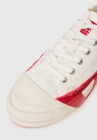 Tenis de canvars cu un superior alb, cu accente roșii, vârf din cauciuc și șireti prin ochiuri de argint. Talpa texturată cu un design stratificat.