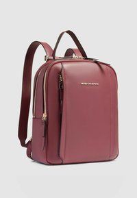 Mochila de cuero burdeos con herrajes dorados, diseño estructurado, doble cremallera y correas ajustables; textura suave con detalles mínimos.