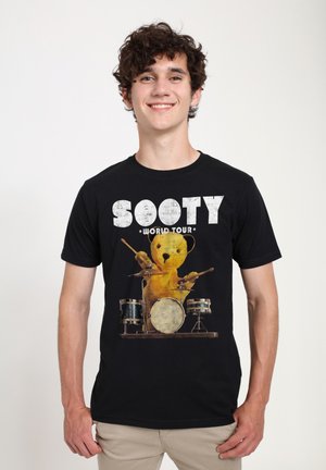 Sort bomulds-T-shirt med et grafisk billede af en gul bjørn, der spiller trommer, og teksten "SOOTY WORLD TOUR" i fed, slidt hvid skrift.