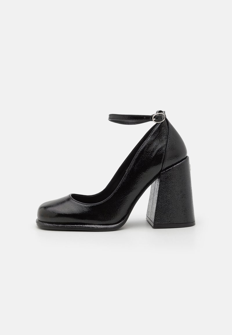 Chaussure à talon haut en cuir verni noir avec bout arrondi, bride à la cheville et talon épais, vue de profil sur fond blanc.