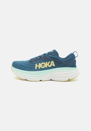Blå løbesko med tyk hvid sål, gul "HOKA"-logo på siden, snørelukning og polstret hælkant med trækskærm.