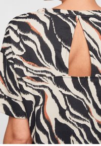 Blusa de manga corta en beige, con un patrón de cebra en negro y naranja. La parte trasera tiene una abertura en forma de llave con una costura a lo largo del escote.