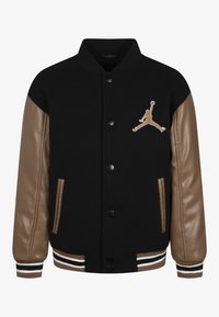 Czarna kurtka varsity z brązowymi skórzanymi rękawami, haftowanym logo Jumpman, zatrzaskami, prążkowanymi ściągaczami przy mankietach i kieszeniami po bokach.