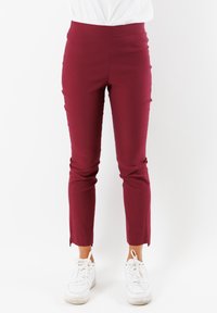 Pantaloni slim-fit color bordeaux con vita alta, caratterizzati da una texture liscia e orli spaccati. Abbinati a sneakers bianche per creare un contrasto.