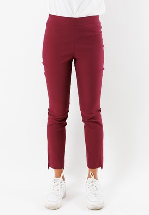 Pantaloni slim-fit color bordeaux con vita alta, caratterizzati da una texture liscia e orli spaccati. Abbinati a sneakers bianche per creare un contrasto.