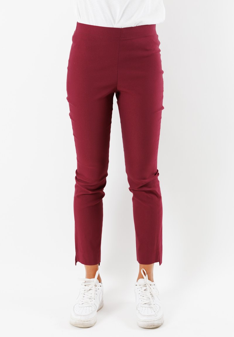Pantaloni slim-fit color bordeaux con vita alta, caratterizzati da una texture liscia e orli spaccati. Abbinati a sneakers bianche per creare un contrasto.