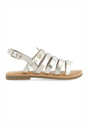 Sandalo strappy metallico argento con punta aperta, cinturino alla caviglia regolabile e suola imbottita. Suola piatta con un sottopiede testurizzato color tan.