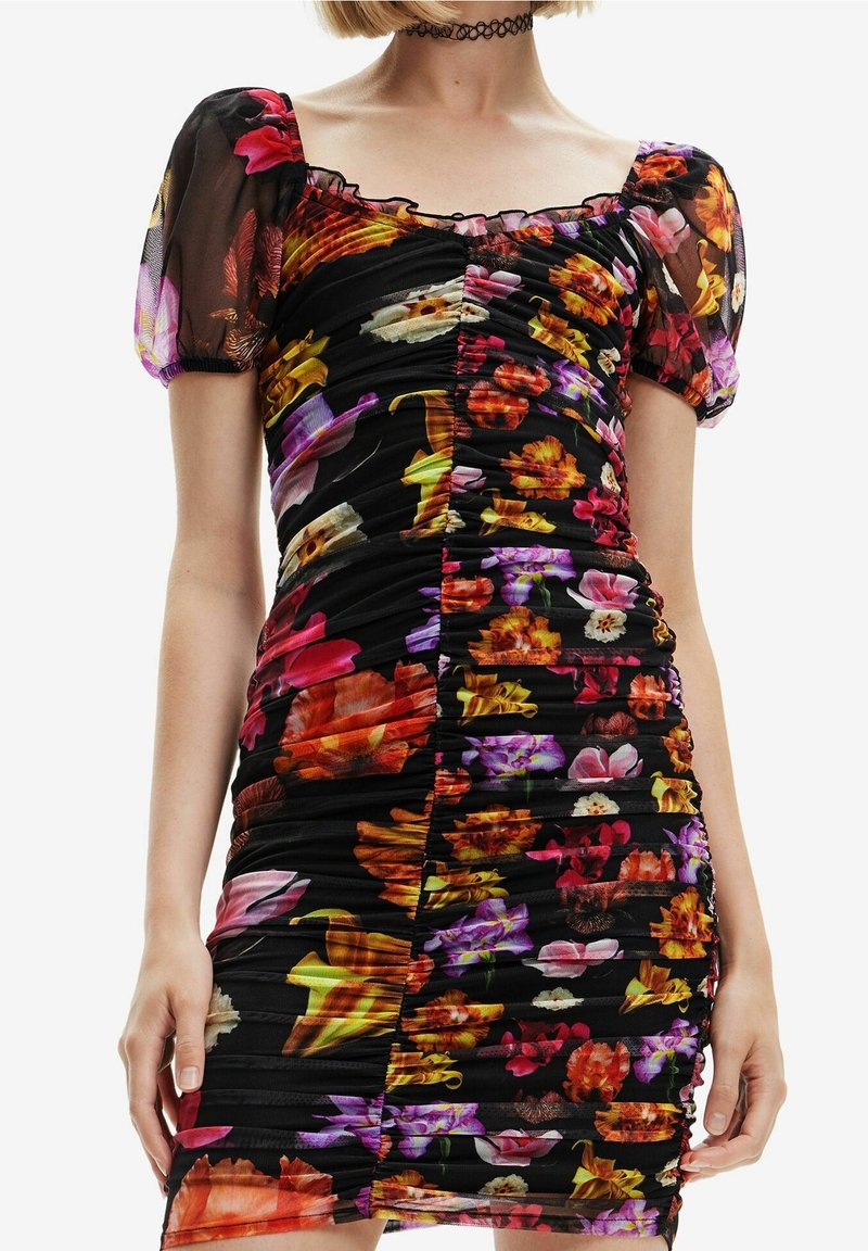 Femme portant une robe noire ajustée avec des détails froncés et un imprimé floral coloré, des manches courtes bouffantes et un collier ras du cou.