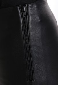 Zwarte leren rok met een zichtbare rits aan de zijkant. De textuur lijkt glad met een lichte glans. Close-up onthult details van de rits.