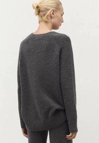 Pull en laine gris avec un ourlet et des poignets côtelés, présentant une coupe décontractée et un col montant. La vue arrière montre une texture lisse et douce.