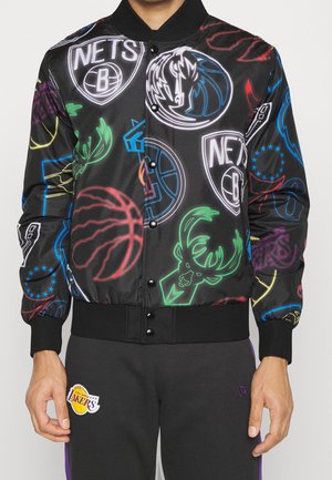 Czarna kurtka bomber z kolorowymi neonowymi logo drużyn NBA, noszona przez osobę w czarnych spodniach z naszywką Los Angeles Lakers.