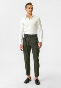 Witte overhemd met knopen, met een slim fit, gecombineerd met olijfgroene op maat gemaakte broeken met plooien en een zijsluiting. Zwarte gevlochten schoenen.