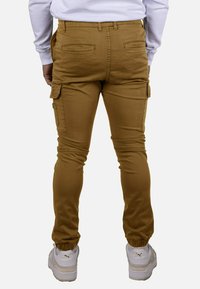 Pantalones cargo caqui de corte ajustado, con bolsillos laterales, puños elásticos y textura suave. Combinados con zapatillas blancas.