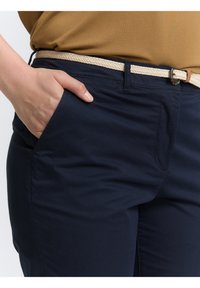Námořnické modré bavlněné kalhoty s přední kapsou, doplněné pleteným krémovým opaskem a rovný střih. Hladká textura bez viditelných vzorů.