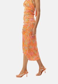 Orange dress with a fitted bodice and a flowy skirt, adorned with pink and blue patterns, paired with matching orange strappy heels.