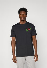 Sort kortærmet t-shirt i bomuld med en farverig grafik af et palmetræ og logo på brystet, kombineret med grå træningsbukser.