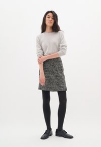 Un pull gris, une jupe texturée à motifs noir et blanc, des collants noirs et des chaussures noires. La tenue présente une silhouette ajustée et des motifs discrets.