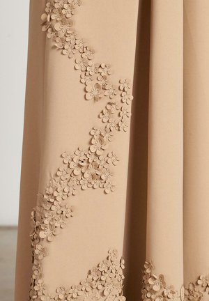 Beige fabric featuring a cascading floral appliqué design with three-dimensional flowers along one side, creating a textured appearance.