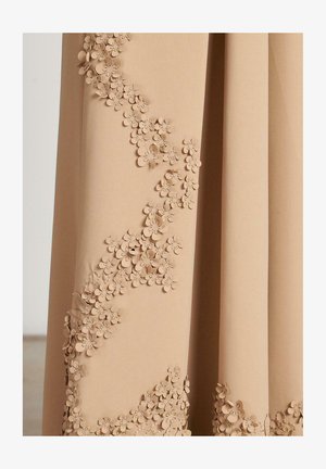 Beige fabric featuring a cascading floral appliqué design with three-dimensional flowers along one side, creating a textured appearance.
