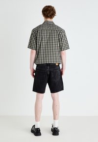 Korte ærmer, ternet skjorte i sort og beige stof, parret med sorte denim shorts. Bagfra vises syede sømme og mærkedetaljer.