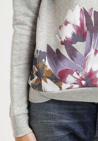 Sweat-shirt gris avec un motif floral en violet, rose et marron. Poignets et ourlet côtelés avec une texture de tissu douce. Coupe classique.