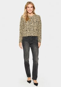 Majica z dolgimi rokavi v leopardjem vzorcu iz mehkega materiala, v paru s temno denim hlačami in črnimi čevlji s koničastim nosom. Neutrala ozadja.