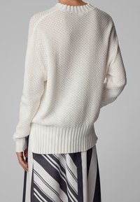 Weißer Strickpullover mit strukturiertem Muster, gerippten Bündchen und Saum sowie einem Rundhalskragen. Die Rückansicht zeigt die lockere, bequeme Passform.