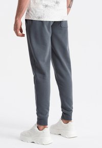 Grå sweatpants med et tætsiddende design, elastiske manchetter og sidelommer, parret med hvide klodsede sneakers, på en ensfarvet baggrund.