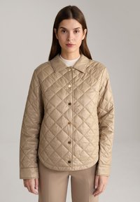 Beige gewatteerde jas met een kraag, voorzien van gouden drukknoopjes en lange mouwen. Gladde textuur en een diamantpatroon over de hele jas.
