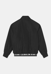 Černá bunda s hladkým povrchem, žebrovanými manžetami a lemem, a kontrastním bílým páskem se textem "CALVIN KLEIN JEANS".