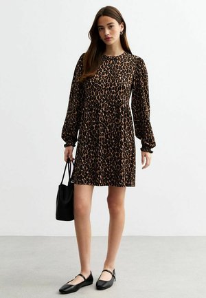 Robe en imprimé léopard avec de longues manches bouffantes, un col rond et une taille froncée. Modèle tenant un sac noir et portant des ballerines noires.