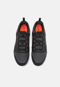 Baskets de sport noires et grises avec tige en mesh et accents oranges. Les caractéristiques incluent un design à lacets, une languette rembourrée et une semelle texturée.