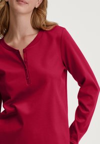 Halfopen, bordeaux overhemd met lange mouwen van zachte stof. Beschikt over een henley-halslijn met drie knopen en een gestructureerde ribbelkraag.