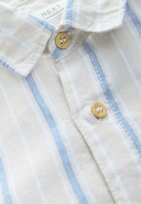 Camicia a maniche lunghe di colore chiaro, a righe, in misto lino, caratterizzata da righe verticali azzurro chiaro e bianche, con bottoni in legno e colletto.