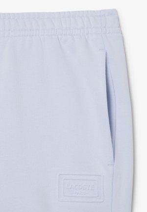 Pantalones deportivos azul claro con cinturilla elástica, bolsillo lateral y logotipo rectangular en relieve de Lacoste Paris cerca del bolsillo.