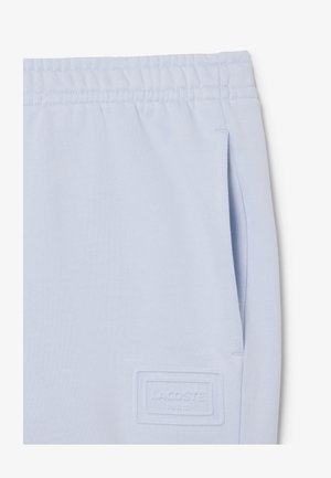 Pantalones deportivos azul claro con cinturilla elástica, bolsillo lateral y logotipo rectangular en relieve de Lacoste Paris cerca del bolsillo.