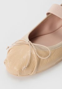 Ballet flat em couro bege claro com acabamento texturizado, tira elástica e laço decorativo. Bico arredondado e forro interior suave.