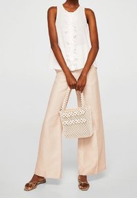 Top blanco sin mangas con delante con volantes, pantalones de pierna ancha de cintura alta en color beige y un bolso crema texturizado con un patrón tejido.