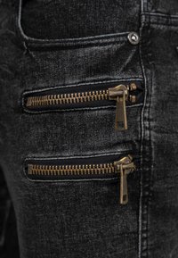 Close-up of two horizontal bronze zippers on black denim fabric with visible stitching and a rivet button.