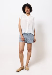 Weißes, kurzärmliges, knopfbares Hemd, kombiniert mit hellblauen Denim-Shorts und tanfarbenen, geschnürten Schuhen; einfaches Design mit geraffter Textur.