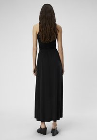 Robe maxi noire avec un buste ajusté, une taille froncée et une jupe fluide. Le tissu semble doux, avec une texture lisse et des détails minimalistes.